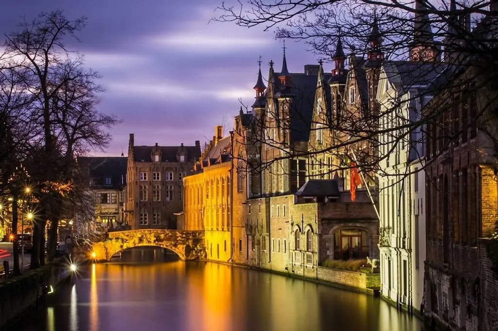 Margem do rio de Bruges iluminada à noite com edifícios refletidos